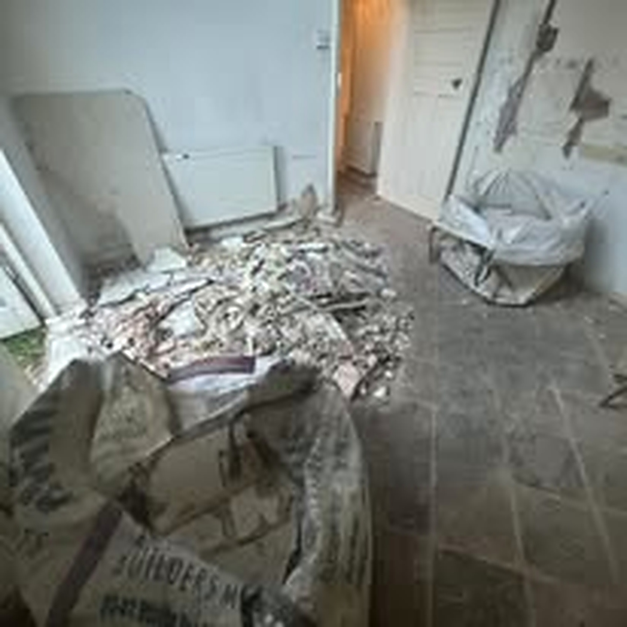 Stripped-out room with plasterboard, rubble and builders waste bags piled on the floor during a renovation