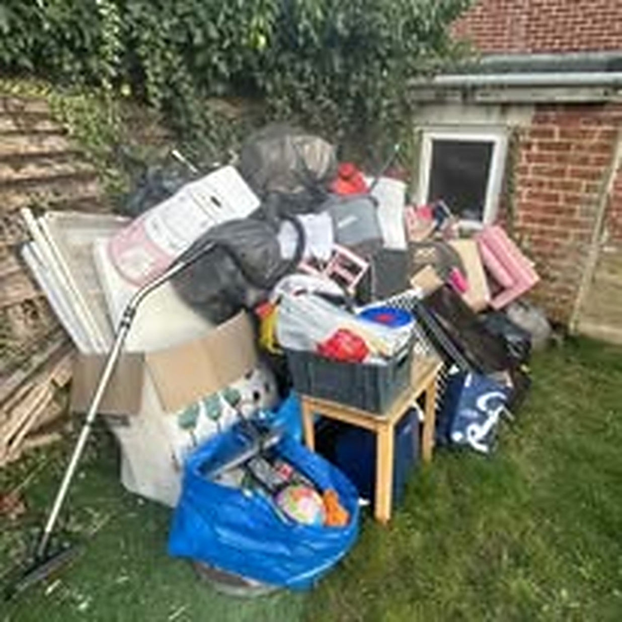 Large pile of bagged household waste, furniture and boxes stacked in a garden before clearance